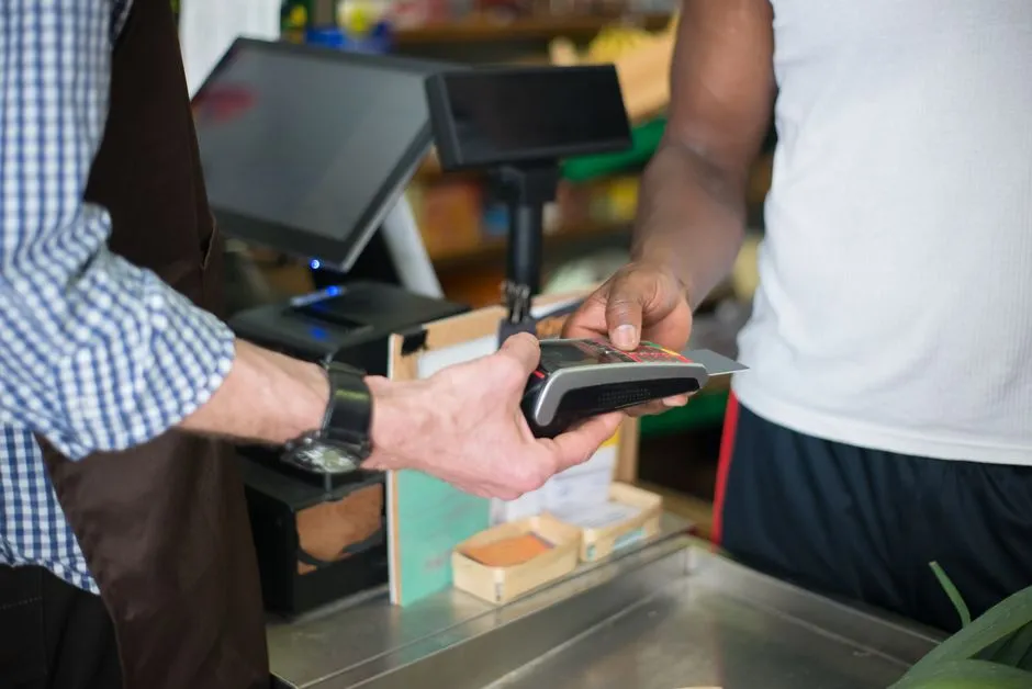 Shopper tapping a payment card on a checkout terminal at a grocery counter